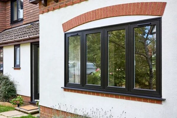 A house exterior with black flush-framed windows set in a white rendered wall with a red brick arch