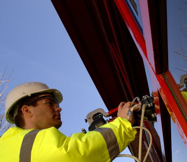 A worker in a hard hat and hi-vis jacket using a suction lifter to install a large window frame