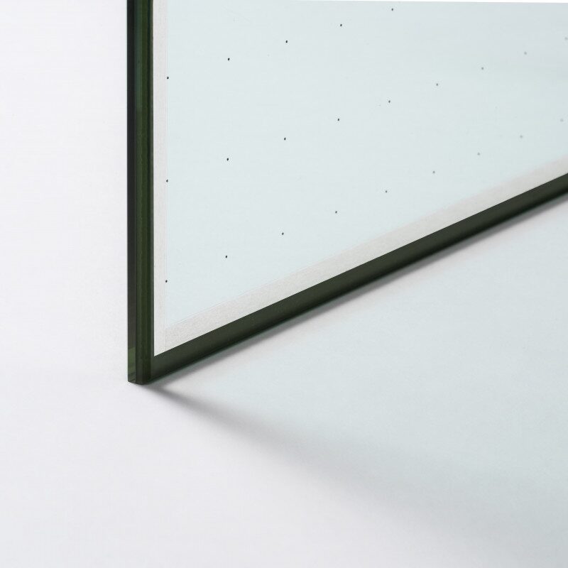 A close-up corner of an insulating glass panel showing its edge and spacer, photographed on a plain white background
