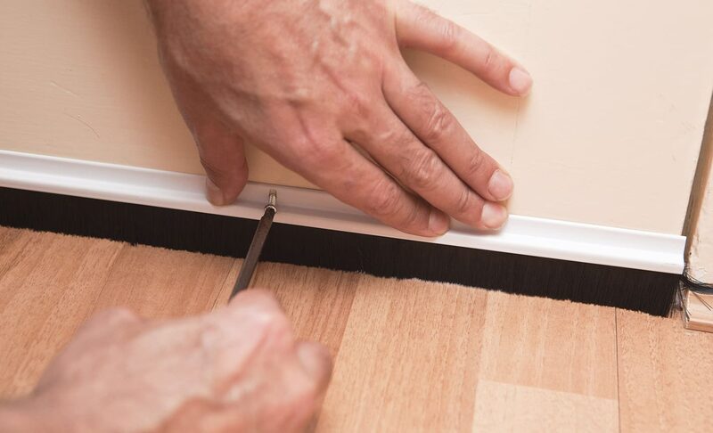 Close-up of hands screwing a brush draught excluder strip to the bottom of an interior door