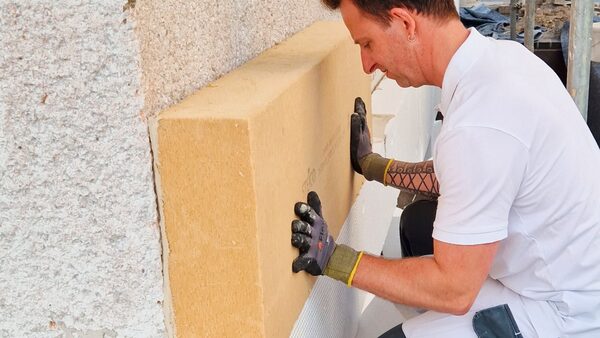 A tradesman fitting a large yellow wood-fibre insulation board against an exterior wall
