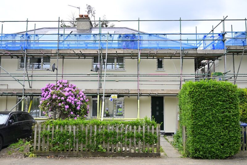 A semi-detached house under scaffolding with blue netting during external wall insulation work