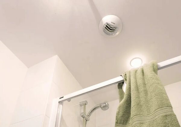 A white ceiling-mounted extractor fan in a bathroom above a shower with a green towel