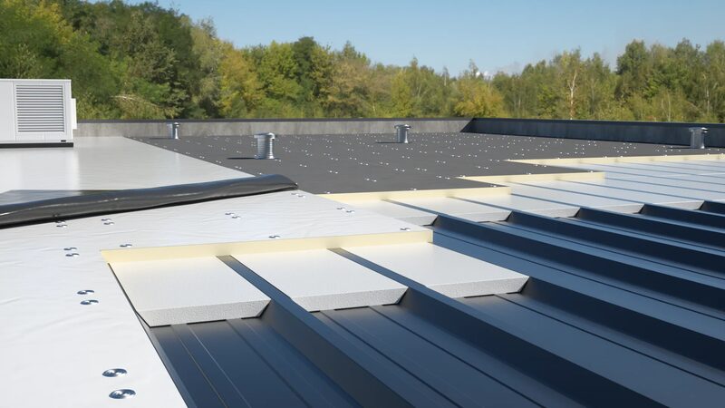 Insulation boards being installed on a flat commercial roof with partially fitted membrane