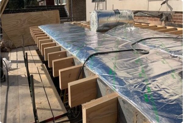 Rolls of reflective foil insulation laid over wooden roof joists on a flat roof under construction