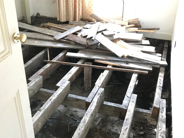 A room with its wooden floorboards ripped up, exposing bare floor joists during renovation work