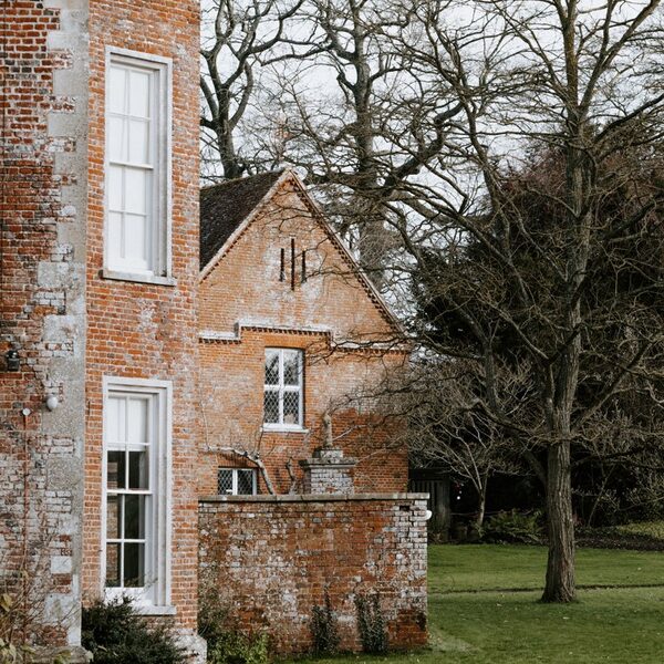 A historic red-brick heritage building with sash windows and a walled garden beside bare trees