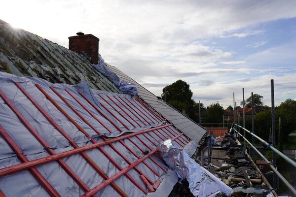 A house roof mid-renovation with reflective foil insulation and red battens being installed over the rafters, with scaffolding alongside