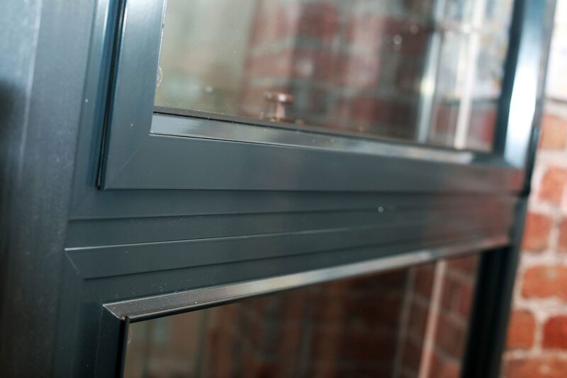 A close-up of dark grey aluminium secondary glazing panels fitted inside a window with a brick wall behind