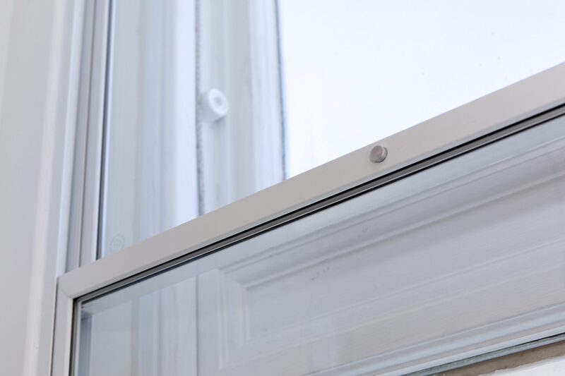A close-up of a white vertical sliding secondary glazing panel installed inside a sash window frame