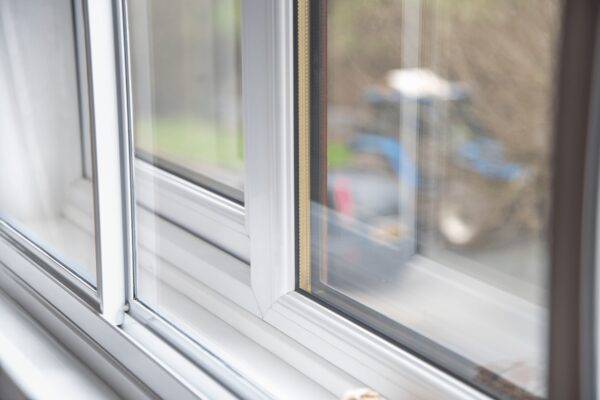 A close-up of a white secondary glazing panel installed inside a window frame, with a blurred garden view outside