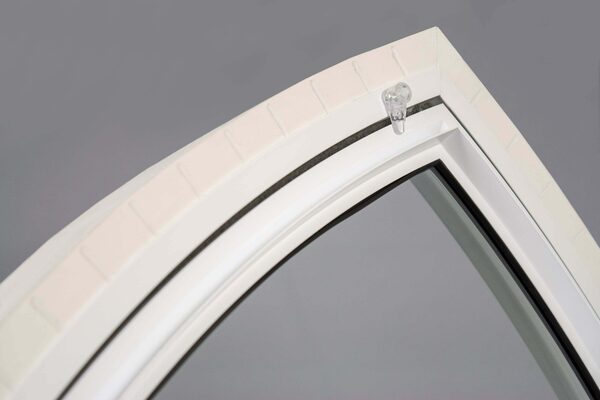 Close-up of a white arched secondary glazing panel fitted inside a brick window reveal, showing the frame and clip fixing