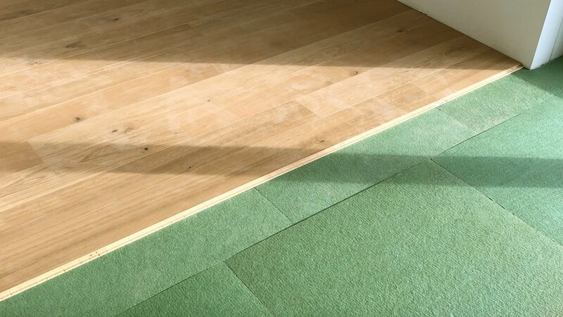 Green wood-fibre insulation boards laid between floor joists next to a wooden floorboard surface