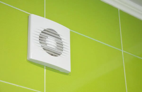 A white bathroom extractor fan mounted on a bright green tiled wall