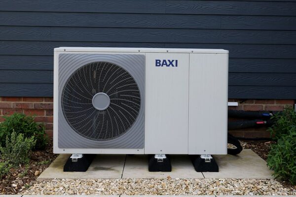 A Baxi air source heat pump unit installed outside a house against a dark grey wall