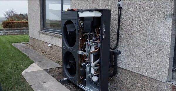 A Panasonic air source heat pump unit installed outside a house, with its side panel open exposing internal components and pipework