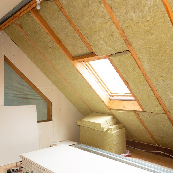Mineral wool insulation batts fitted between the rafters of a loft conversion with a Velux-style roof window and plasterboard stacked below