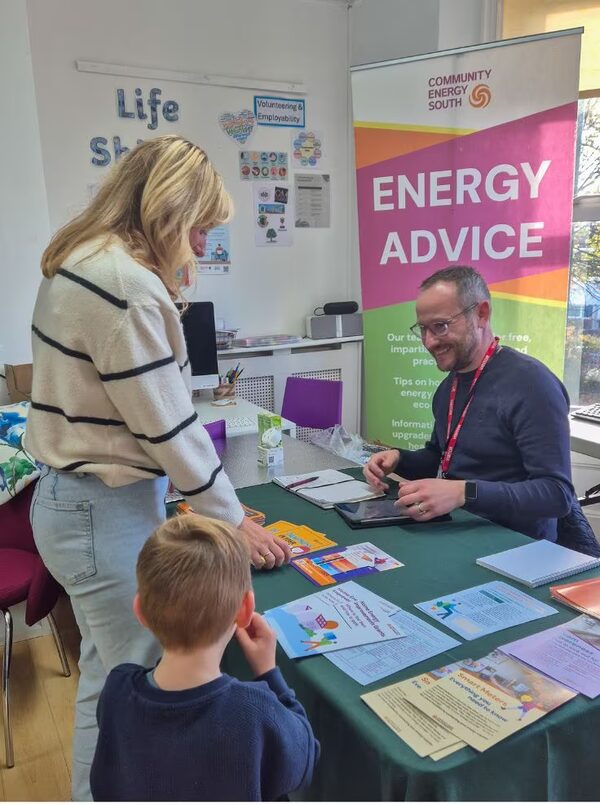 A Community Energy South adviser at an energy advice stall talking with a woman and child over leaflets on a table