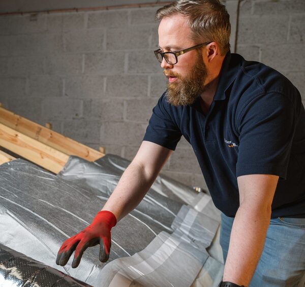 A workman fitting foil-backed multifoil insulation between rafters in a loft