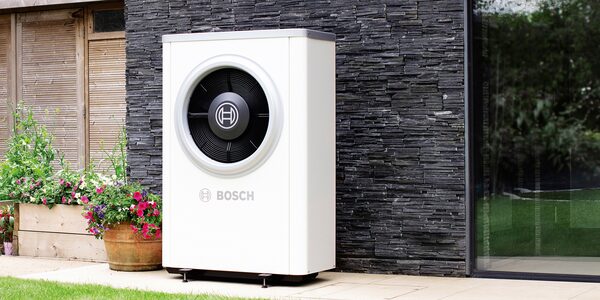 A white Bosch air source heat pump unit installed outside a house next to a flower planter