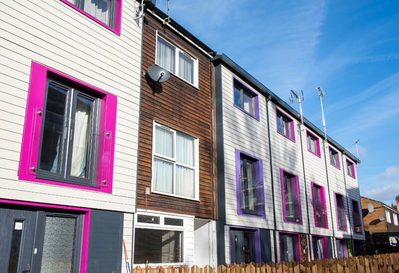 A row of retrofitted terraced houses with external wall insulation cladding in white, grey and timber finishes with bright pink and purple window surrounds