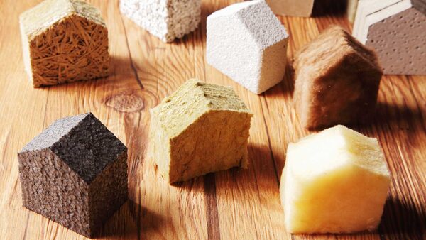 Small house-shaped samples of different insulation materials, including mineral wool, foam and wood fibre, arranged on a wooden surface