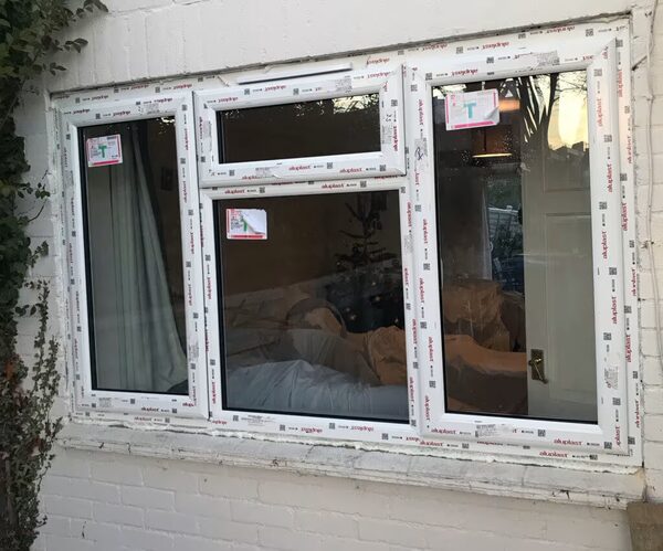 A newly installed Anglian uPVC window still covered in protective film, fitted in the white brick exterior wall of a house