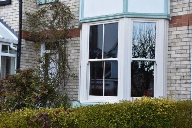A white Victorian sash bay window installed on a brick house exterior