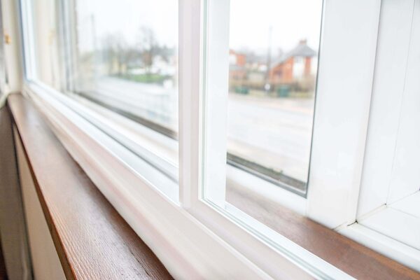 A close-up of white horizontal sliding secondary glazing panels fitted inside a window with a wooden sill
