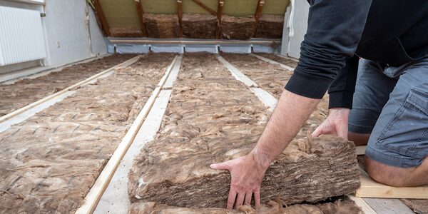A person laying mineral wool loft insulation between joists in an attic