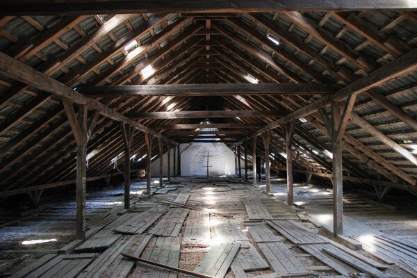 An empty uninsulated loft space with exposed wooden roof beams and scattered floorboards
