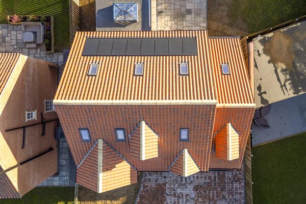 Aerial view of a house roof with clay tiles and a row of black solar panels on the rear slope