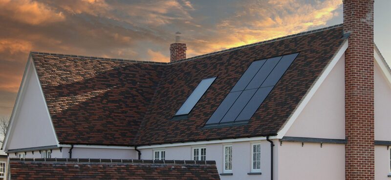 A house roof at sunset with dark solar tiles integrated into the tiled roof alongside a rooflight