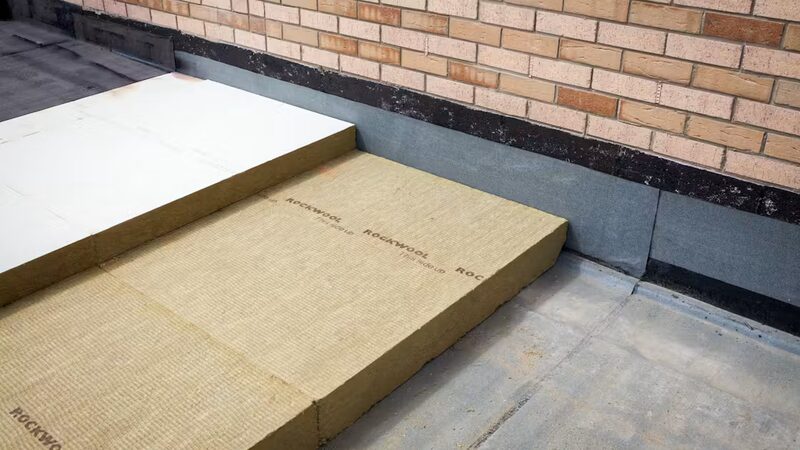 Rockwool stone wool insulation boards being installed on a flat roof against a brick wall