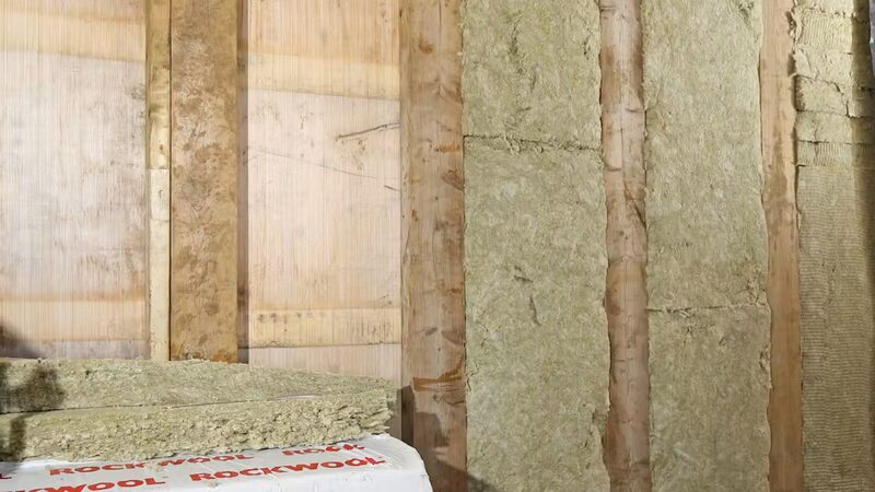 Rockwool stone wool insulation slabs fitted between timber studs in a partially insulated wall, with wrapped Rockwool slabs in the foreground