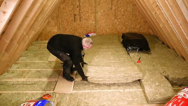 A man laying a mineral wool insulation roll between joists in a loft