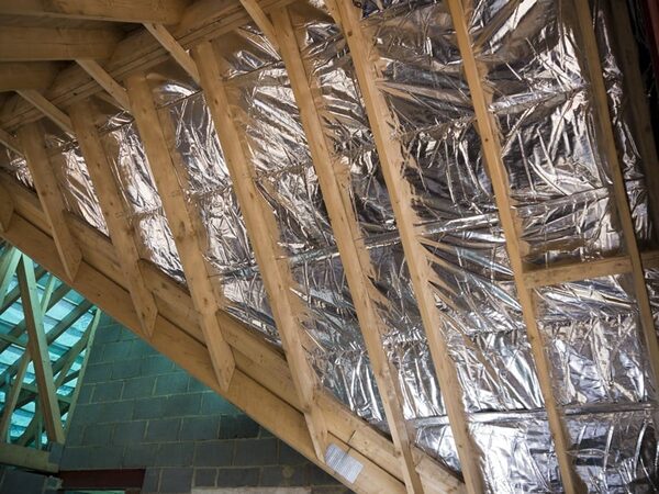 Shiny multifoil insulation fitted between the wooden rafters of a sloping roof under construction