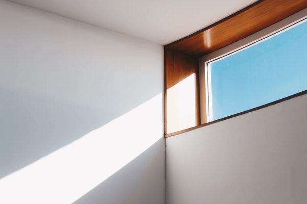 Sunlight streaming through a wooden-framed window into a white-walled room corner
