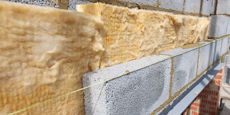 Yellow mineral wool insulation batts fitted between concrete blockwork on a partially built cavity wall