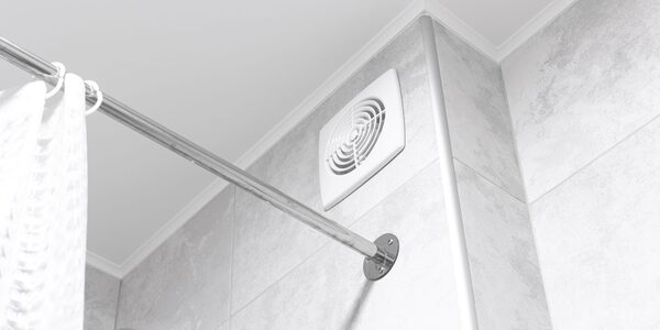 A white ceiling-mounted bathroom extractor fan on a tiled wall next to a chrome shower curtain rod