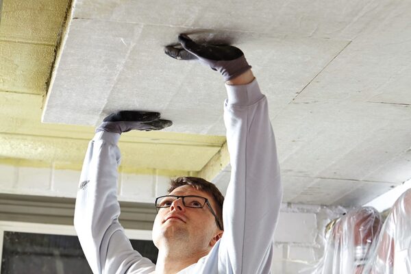 An installer fitting a ROCKWOOL stone wool insulation board to a basement ceiling