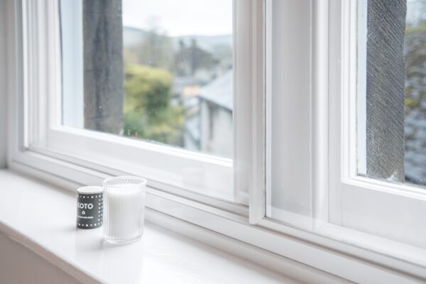 A white horizontal sliding secondary glazing panel installed on a sash window, with a candle on the windowsill