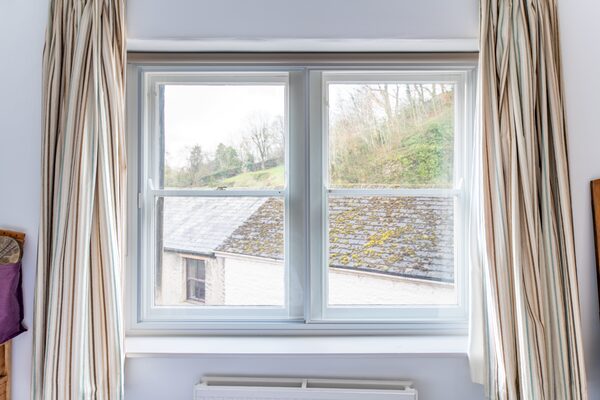 A white horizontal sliding secondary glazing panel fitted inside a sash window in a room with striped curtains