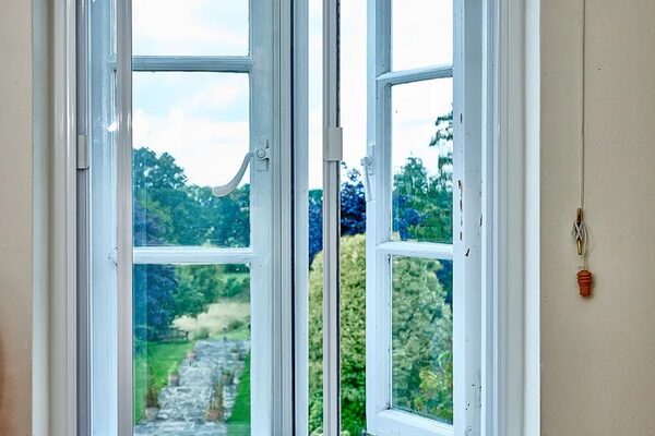 A white secondary glazing panel installed inside an open casement window overlooking a garden