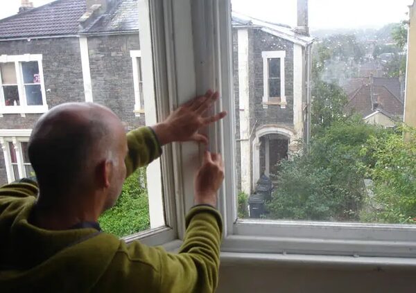 A man fitting secondary glazing to a sash window overlooking terraced houses