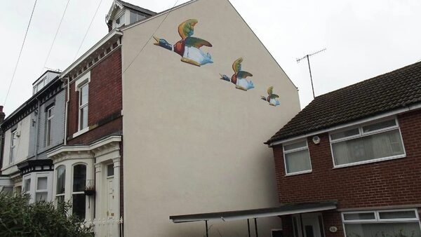 A terraced house with a smooth cream external wall insulation finish decorated with painted flying ducks, next to brick neighbours