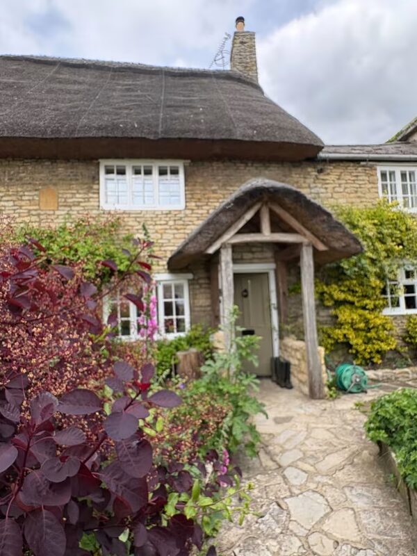 A traditional 18th century stone cottage with a thatched roof, timber porch and garden plants