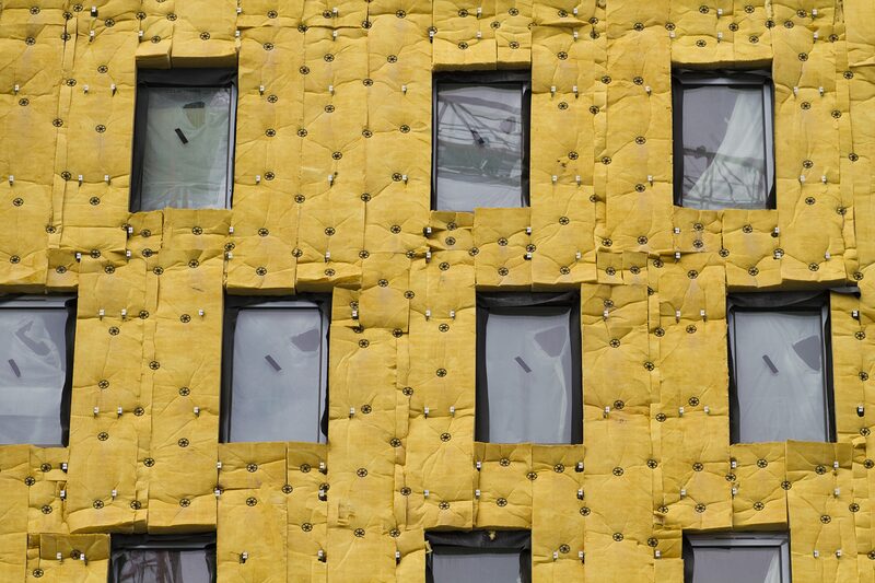 A building facade covered in yellow mineral wool insulation panels with windows, during external insulation works
