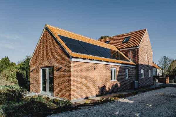 A brick house with solar panels on its tiled roof and a heat pump unit at the side