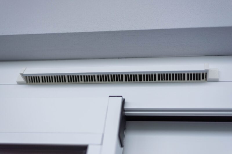 A white trickle vent fitted along the top of a white window frame